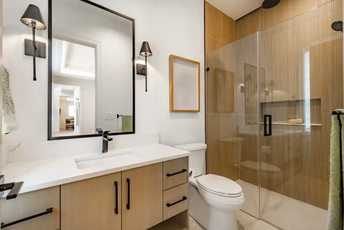 Modern three-piece bathroom with wood vanity and glass shower inside a garden suite in Toronto